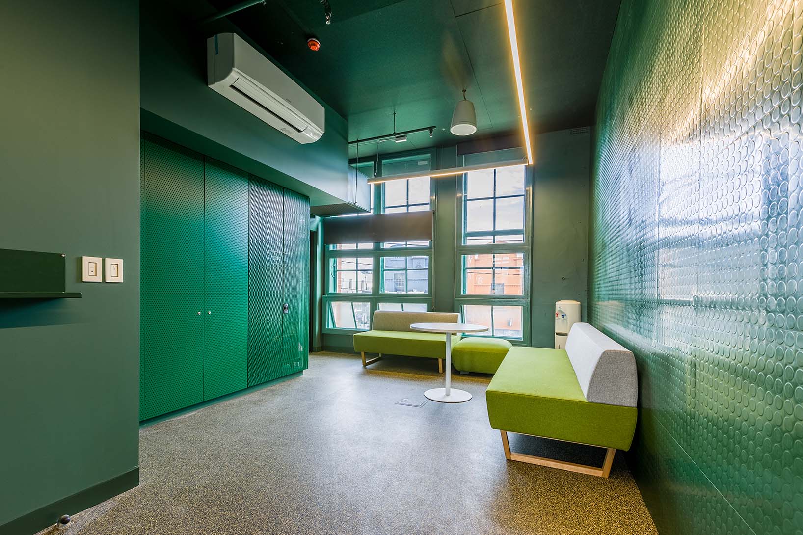 Meeting room with dark green walls, windows and light green and grey couches in the corner.