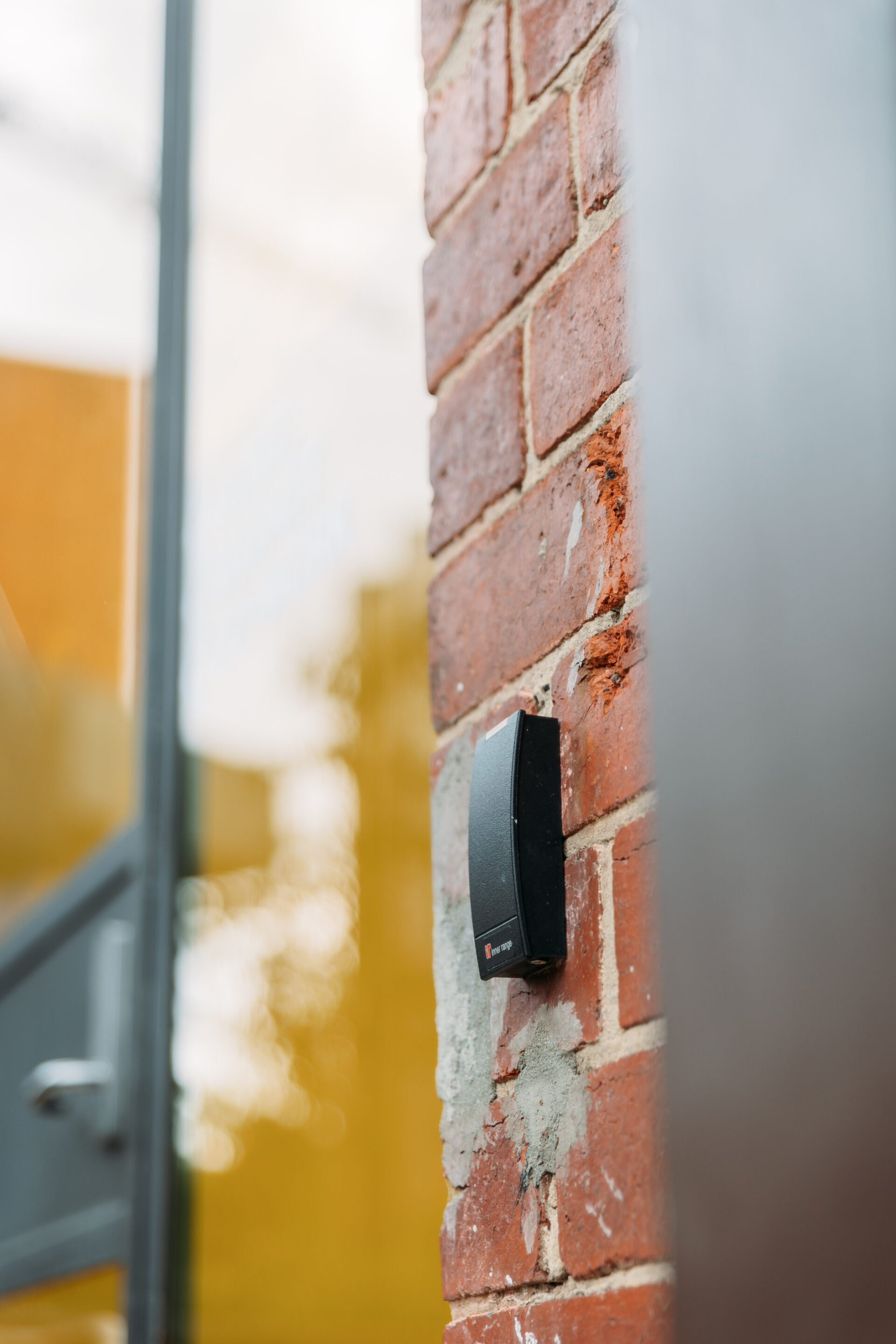Photo of Music Market security entry. To the left is a blurred glass door and door handle. In the foreground is a security swipe pass on a brick wall.